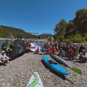 Over 50 rafters gather around the shore of the river with various banners calling for undamming the Eel River.